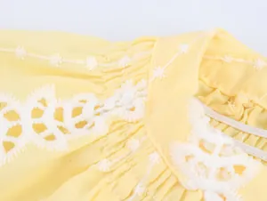 Détail macro de la broderie florale blanche sur une blouse jaune de style français chic