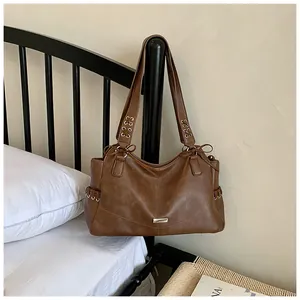 Gros plan d'un grand sac cabas en similicuir marron avec détails d'œillets posé sur un lit