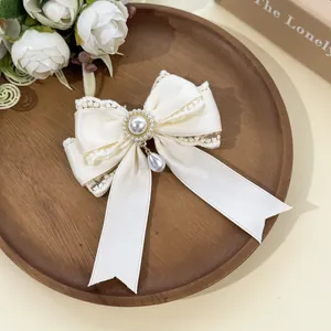 Detail view of elegant cream lace bow hair clip featuring a dangling pearl pendant design