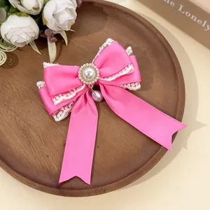 Detailed macro view of a pink satin bow hair clip with white lace trim and pearl pendant