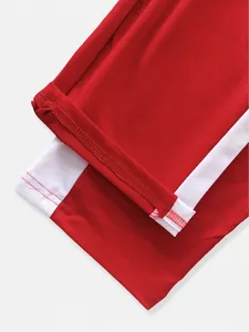 Macro detail shot of red athletic pants hem featuring white side stripe and stitching