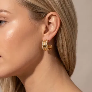 Close-up of elegant gold C-shaped hoop earrings with four rows of sparkling pavé stones on a model.