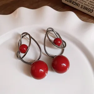 Eleganti orecchini a cerchio in metallo intrecciato con due perle rosse molto lucide