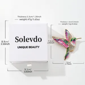 Detailed view of a colorful hummingbird brooch with rhinestones and a white gift box