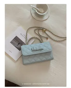 Dettaglio di una borsa a mano trapuntata celeste con fiocco e tracolla a catena d'oro.
