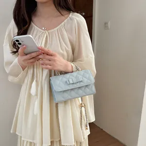 Elegante borsa a tracolla trapuntata azzurra con fiocco e catena dorata indossata da modella
