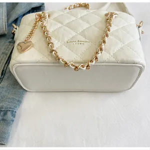 Vue détaillée d'un sac seau matelassé blanc avec poignée chaîne dorée et breloque en forme de cœur