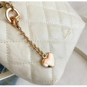 Détail d'un sac en cuir matelassé blanc avec un élégant pendentif cœur doré en chaîne