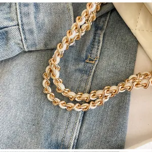Détail de la bandoulière en chaîne dorée entrelacée de cuir blanc sur un sac matelassé