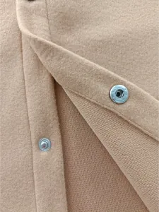 Close-up of camel wool cardigan jacket showing silver snap button and premium fabric texture.