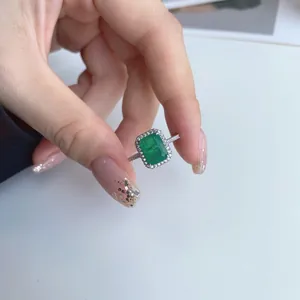 Close-up of elegant emerald cut green gemstone ring with halo design held by hand