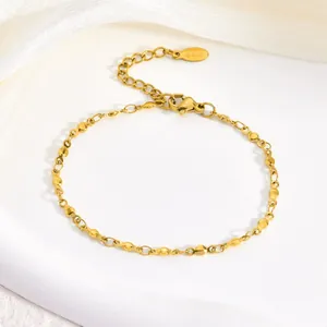 Close-up of a gold stainless steel bracelet with small round disc charms on a white base