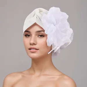 Detailed macro shot of elegant white turban hat featuring a large decorative fabric flower.