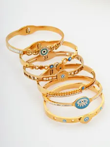 Dettaglio di bracciali rigidi in acciaio titanio placcati oro con vari motivi Malocchio e pietre