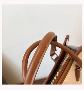 Close-up of brown leather handles and zipper detail on a stylish canvas tote bag.
