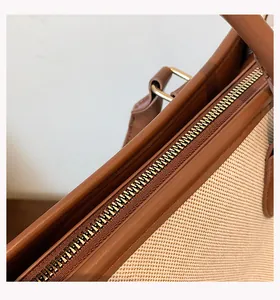 Close-up of smooth gold zipper and brown leather trim on canvas tote bag