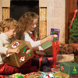 Children decorating gift boxes with festive Christmas cartoon stickers by a fireplace