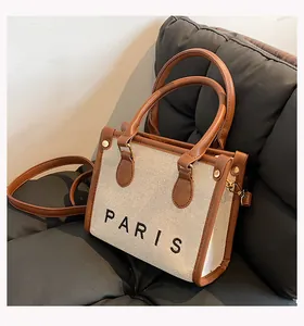 Close-up detail of a structured canvas handbag with brown leather trim and PARIS print.