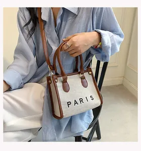 Woman sitting and holding a canvas tote bag with PARIS lettering and brown leather trim