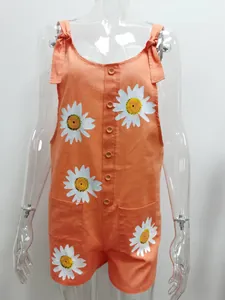 Close-up detail of white daisy floral print on orange cotton linen overalls for women