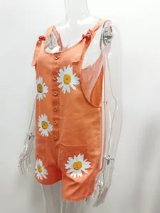 Detailed shot of an orange cotton linen romper with large daisy prints and tie straps