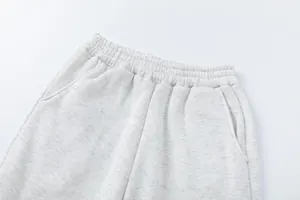 Dettaglio ravvicinato di elastico in vita e tasche su pantaloni sportivi grigio chiaro.