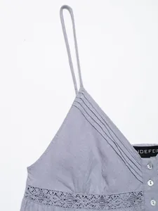Detail view of a light purple camisole with thin straps, pleats, lace, and buttons.
