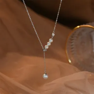Gros plan d'un élégant collier lariat en perles avec chaîne argentée et pompon