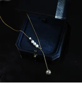 Vue détaillée d'un collier à pompon en perles dorées posé sur un écrin en velours bleu
