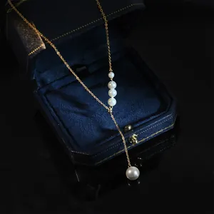 Élégant collier en Y en perles dorées avec pompon présenté sur une boîte à bijoux bleue de luxe