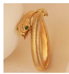 Detailed macro view of a gold snake wrap bracelet featuring green zircon eyes.