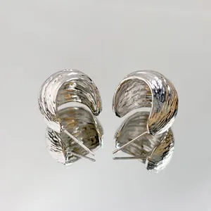 Close-up of silver-toned textured geometric C-shaped stud earrings with a mirrored reflection