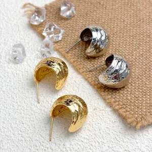 Detail view of gold and silver textured geometric wrinkled stud earrings on natural burlap cloth