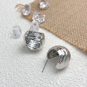 Close-up of silver geometric wrinkled earrings with textured surface on rustic background