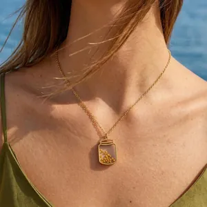 Gold stainless steel mustard seed jar pendant necklace on model with beach background