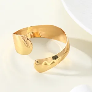 Macro view of a minimalist wide cuff bracelet in polished gold with a smooth water-drop shape