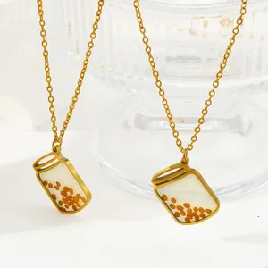 Detailed macro view of mustard seed glass jar pendant on gold stainless steel chain