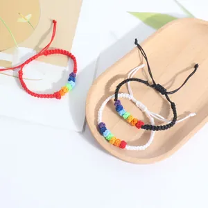 Hand-woven rainbow knot bracelets in red, white, and black displayed on a wooden tray