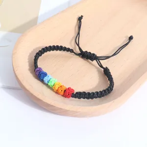 Close-up detail of a handmade rainbow knot woven bracelet displayed on a rustic wooden tray