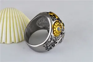 Détail d'une bague tête de mort en acier titane punk avec yeux verts et gravure dorée.