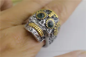 Gros plan d'une bague crâne punk en acier titane avec yeux verts et gravures dorées