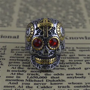 Bague punk en acier titane avec tête de mort, yeux rouges et détail croix dorée