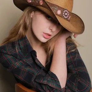 Close-up view of a model wearing a brown straw cowboy hat with floral embroidery