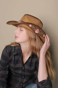 Detailed side view of a straw cowboy hat with elegant floral embroidery on the brown band