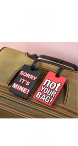 Detailed view of black and red PVC luggage tags with funny slogans on a brown suitcase.