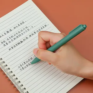 A minimalist Morandi green retractable 0.5mm gel pen being held over a lined notebook