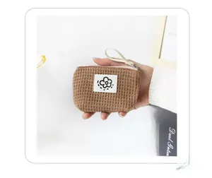 Detail view of a brown waffle-knit mini pouch with a flower tag held in hand for scale