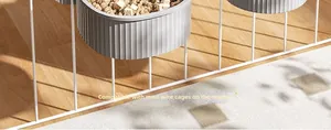 Detail of a grey ribbed hanging pet feeder attached to a white wire cage on wooden floor.