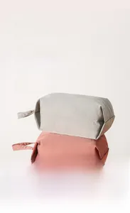 Pila de tres bolsas de viaje de colores en gris, rosa y amarillo de tela lavada suave.