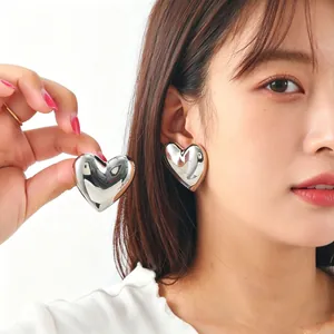 Close-up of large polished heart-shaped silver stud earrings on a model
